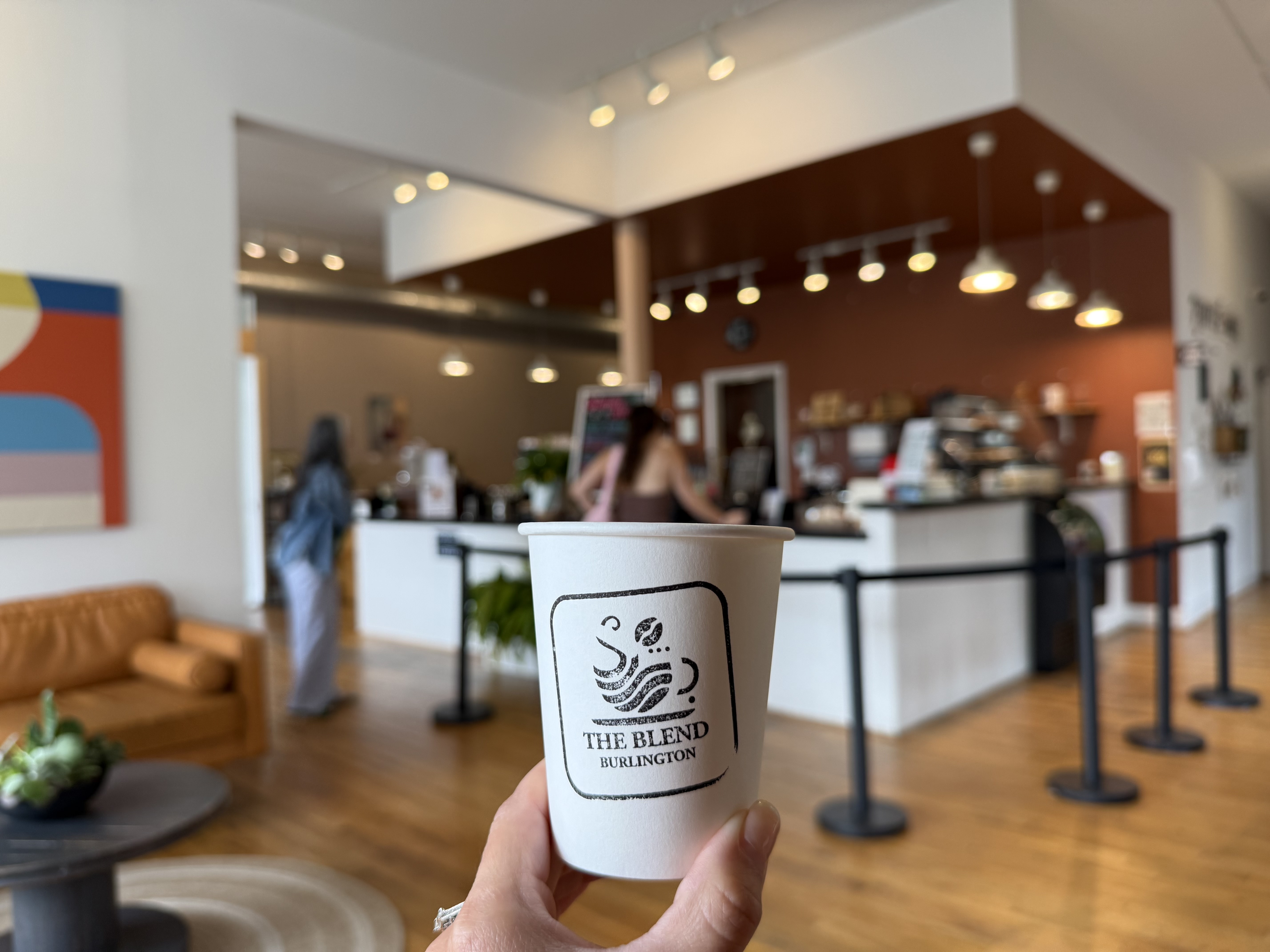 The Blend Burlington coffee cup held in front of the coffee shop interior